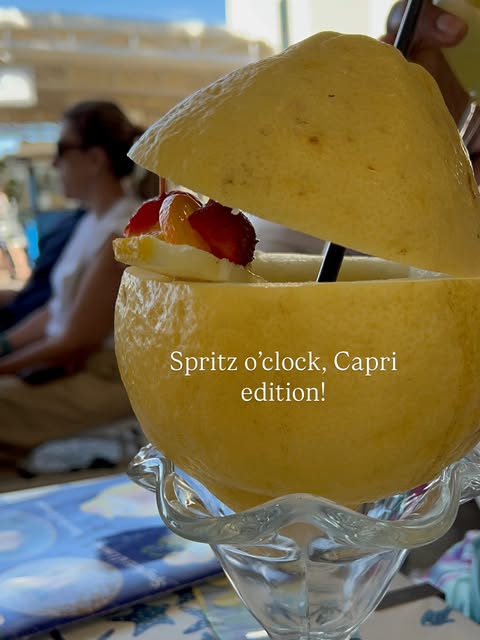 A spritz cocktail served in a hollowed-out lemon with strawberries, enjoyed in Capri